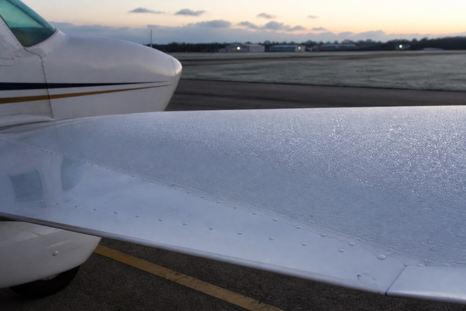 Illustrative close-up of a thin sparkling frost layer on a small aircraft wing with the fuselage visible for context.